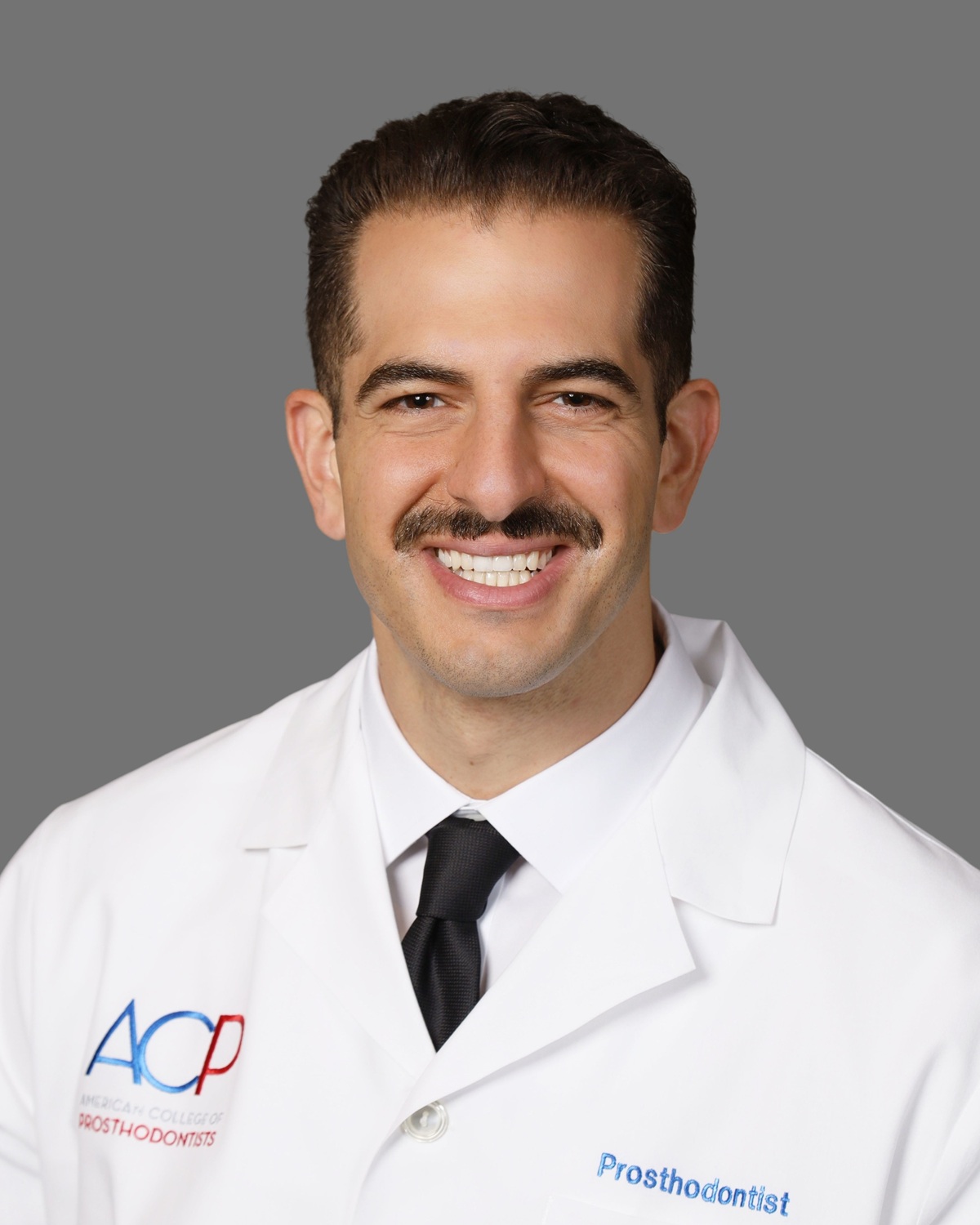Dr. Justin W. Nichols, DDS, MS, prosthodontist, in a white coat with American College of Prosthodontists insignia